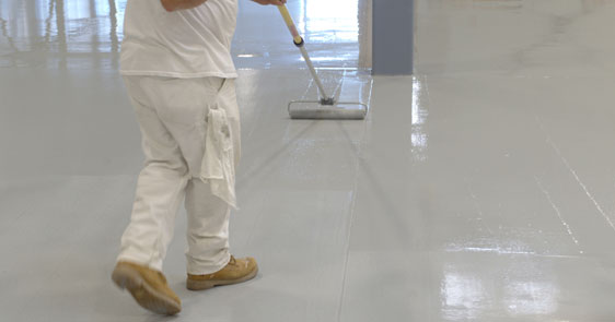This image shows a man applying epoxy paint on an industrial floor.