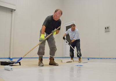 This image shows 2 men applying epoxy paint on an industrial floor.